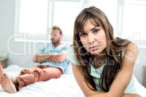Upset woman sitting while man in background on bed
