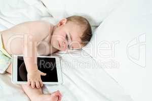 Baby boy lying on bed with digital tablet