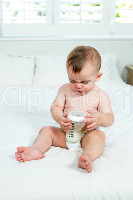 Baby boy sitting with milk bottle on bed at home