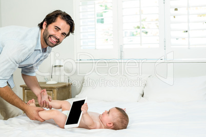 Father playing with son holding digital tablet on bed