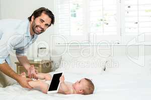 Father playing with son holding digital tablet on bed