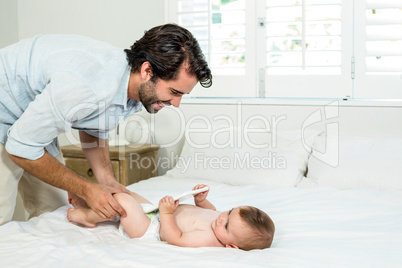 Father playing with baby boy lying on bed