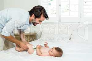 Father playing with baby boy lying on bed