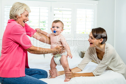 Grandmother and mother holding baby boy on bed