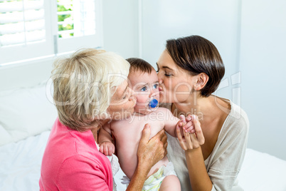 Grandmother and mother kissing baby boy on bed