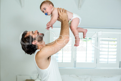 Father playing with son by bed at home