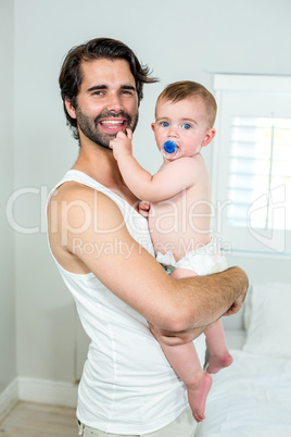 Happy father carrying baby son by bed at home