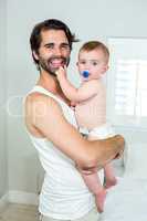 Happy father carrying baby son by bed at home