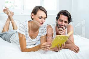 Couple reading book while lying on bed