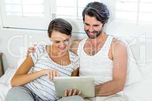 Couple using digital tablet while resting on bed