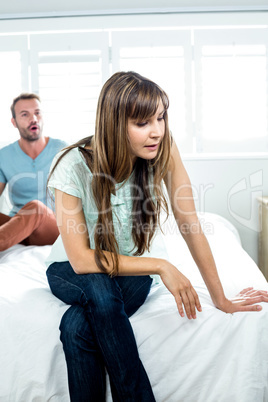 Annoyed woman sitting on bed while man shouting in background