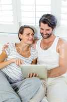 Smiling couple using digital tablet on bed