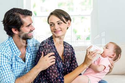 Parents feeding milk to son while sitting on sofa