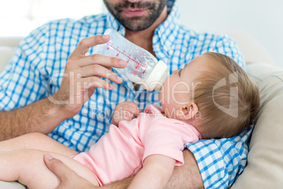 Father feeding milk to son on sofa