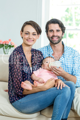 Happy parents feeding milk to son while relaxing on sofa