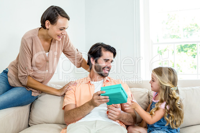Mother and daughter beside man with gift on sofa