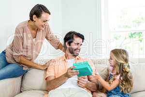 Mother and daughter beside man with gift on sofa