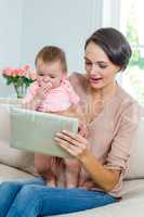 Mother showing digital tablet to son while sitting on sofa