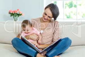 Mother showing picture book to son on sofa
