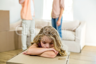 upset girl leaning on box while parents in background