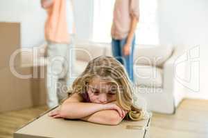 upset girl leaning on box while parents in background