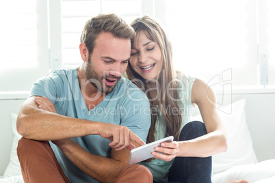 Couple looking in mobile phone while sitting on bed