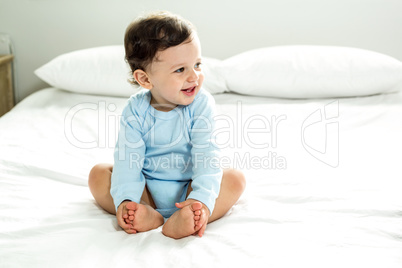 Baby boy smiling while sitting on bed at home