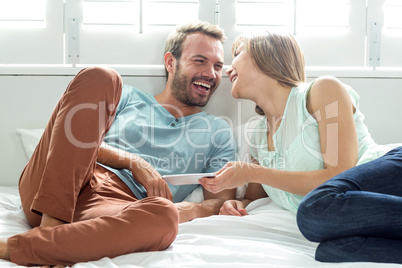 Couple with mobile phone laughing while relaxing on bed