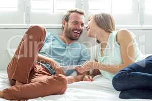 Couple with mobile phone laughing while relaxing on bed