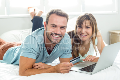 Happy couple online shopping while relaxing on bed