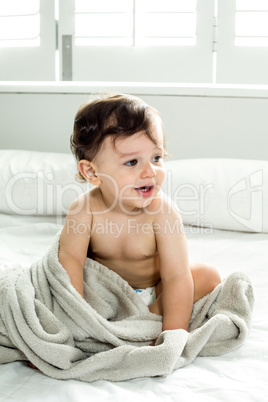 Shirtless baby boy playing with towel on bed