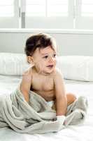Shirtless baby boy playing with towel on bed