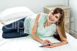 Woman using digital tablet while relaxing on bed
