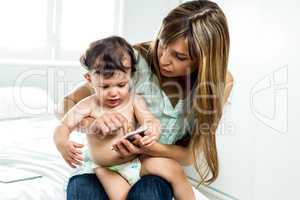 Mother showing cellphone to son while sitting on bed