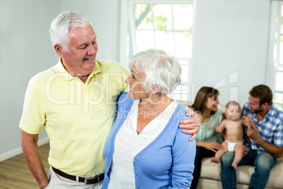 Senior couple with family sitting on sofa in background