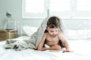 Baby boy covered with towel playing with digital tablet on bed