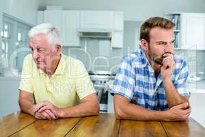 Tensed father and son sitting at table in kitchen