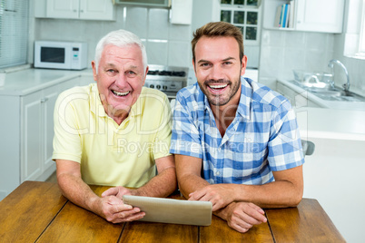 Happy father and son using digital tablet at table in kitchen