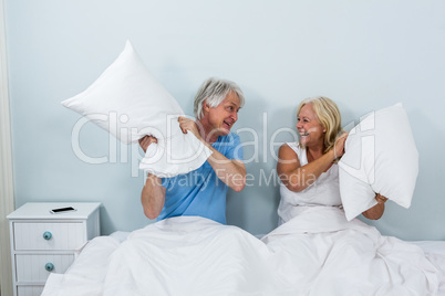 Happy senior couple playing with pillows in bedroom