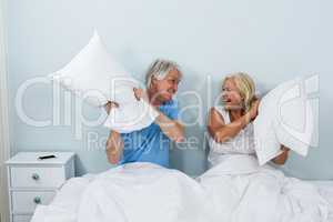 Happy senior couple playing with pillows in bedroom