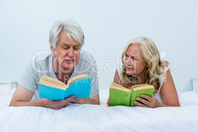 Senior couple reading books while relaxing on bed