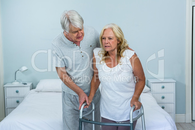 Senior man helping woman to walk in bedroom