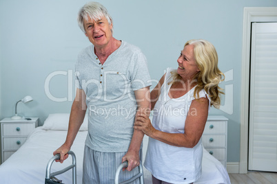 Happy senior woman helping man to walk in bedroom