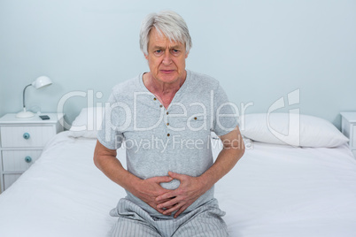 Sad senior man touching stomach at home