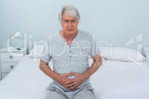Sad senior man touching stomach at home