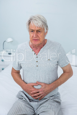 Senior man touching stomach while sitting on bed