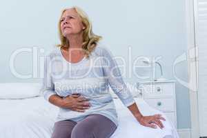 Woman sitting on her bed has stomach ache