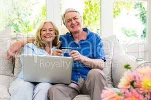 Happy senior couple holding smart card with laptop while sitting