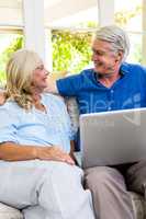 Happy senior couple with laptop while sitting on sofa at home