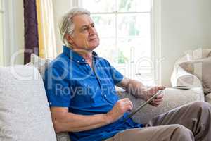 Thoughtful senior man using digital tablet at home